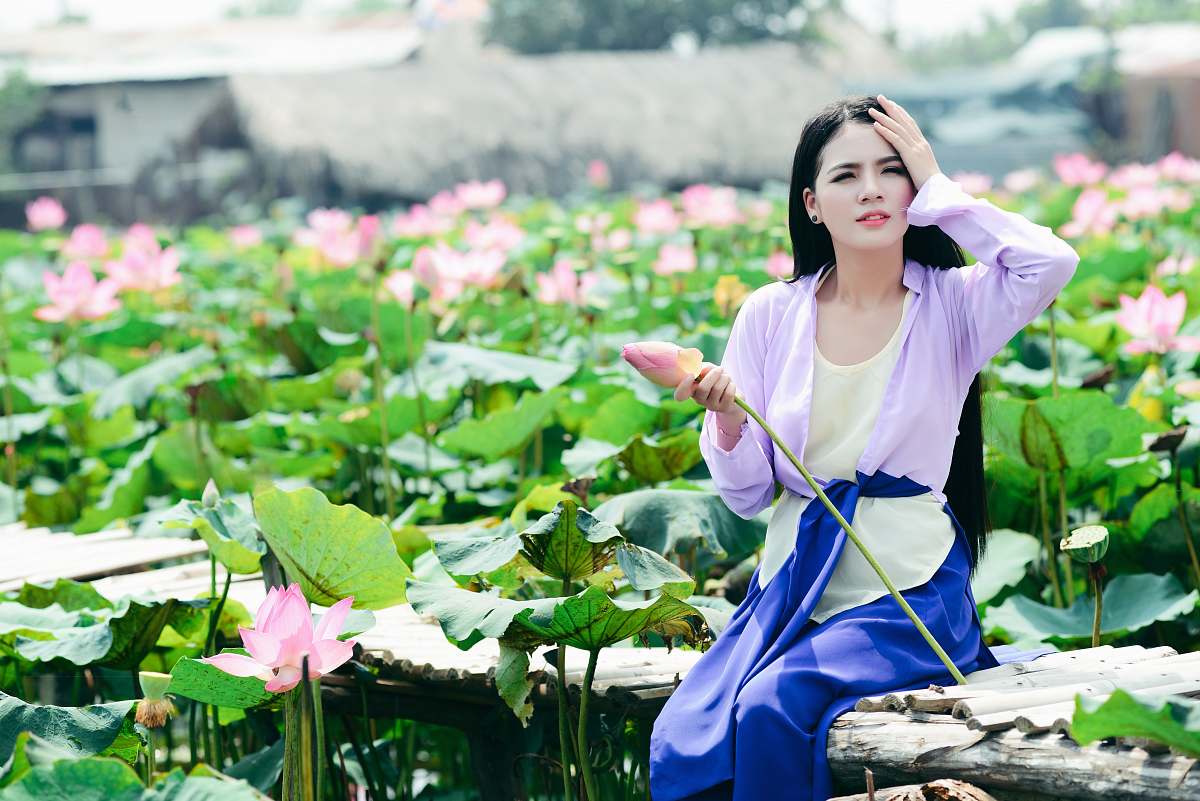 person tilt shift photography of woman sitting behind pink flower plants human