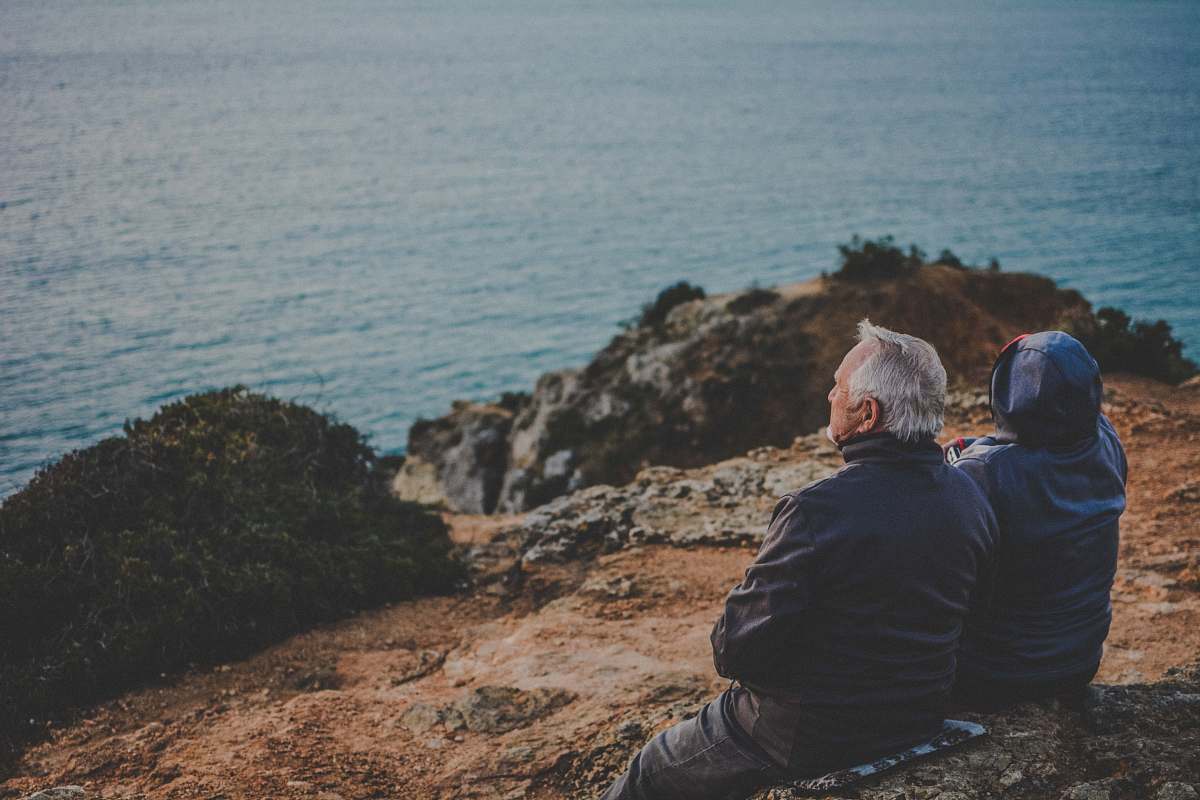 person two person sitting on rock staring at body of water during daytime human