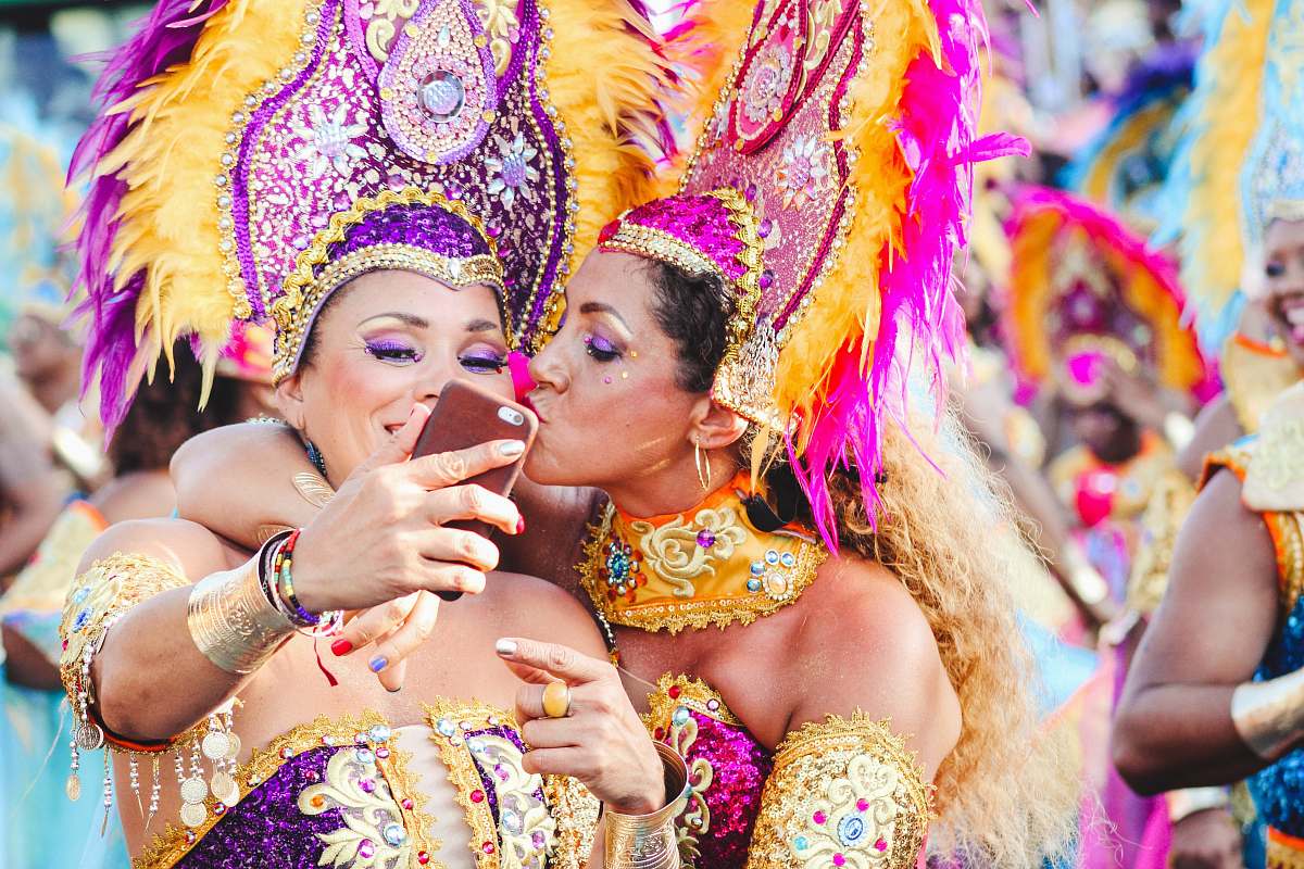 human Two women Carnival dancers pose for a selfie as one kisses other on the cheek. festival