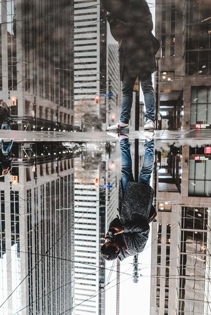 person water mirror reflection photography of man standing on pavement front of buildings human