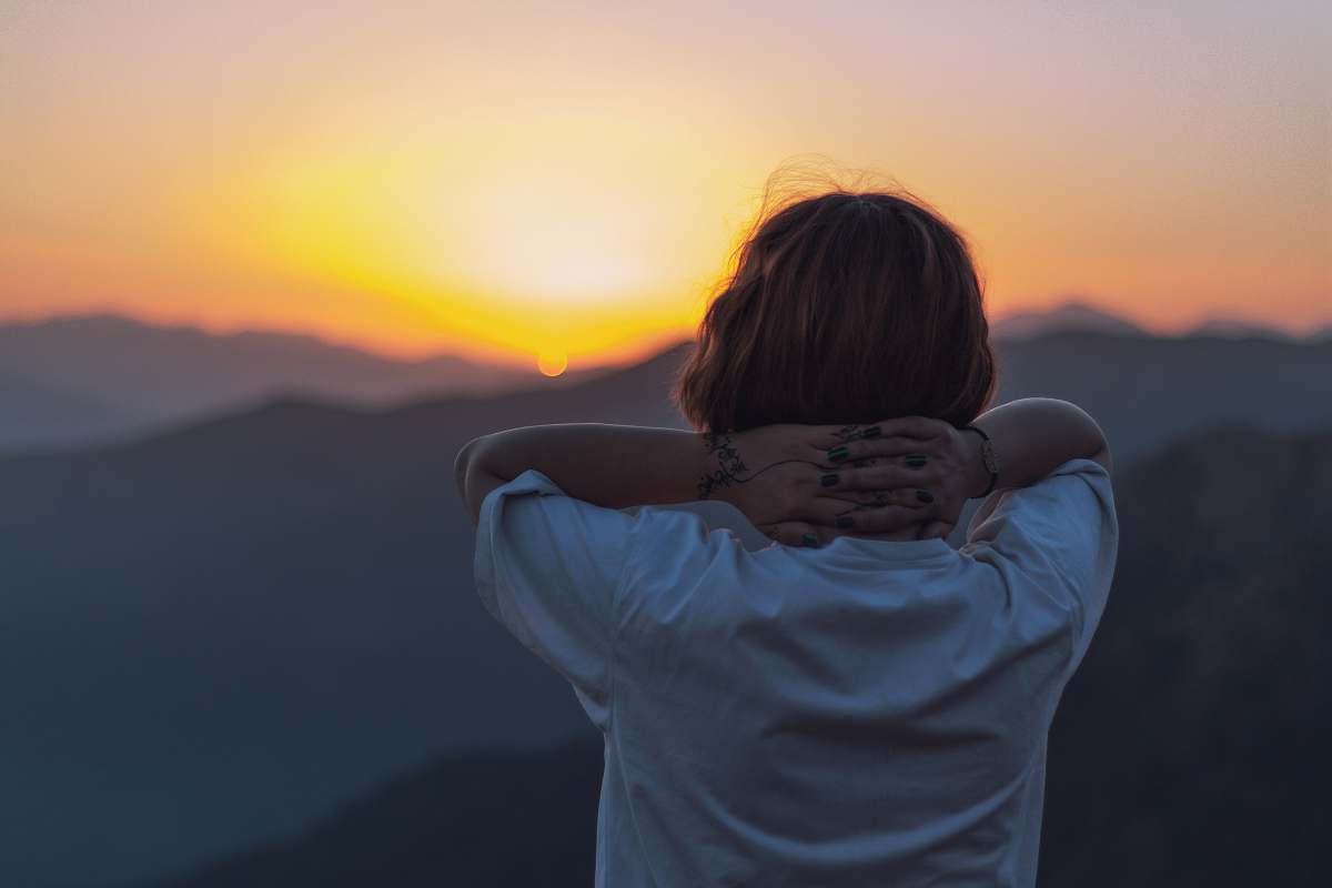 human woman facing backward holding head facing sunset person