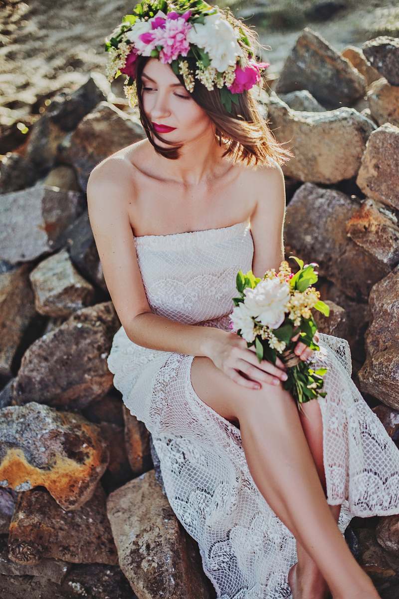 human woman in white tube dress sitting on rock wedding