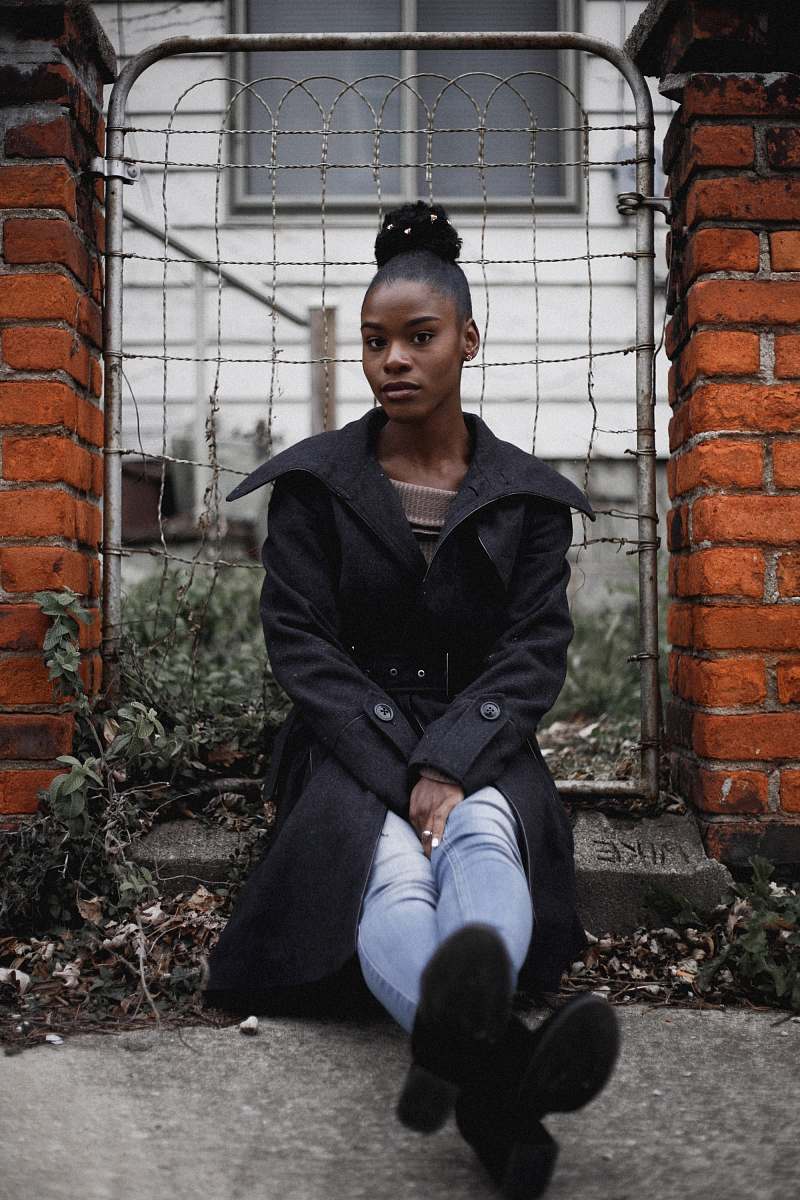 person woman sitting near grey gate brick