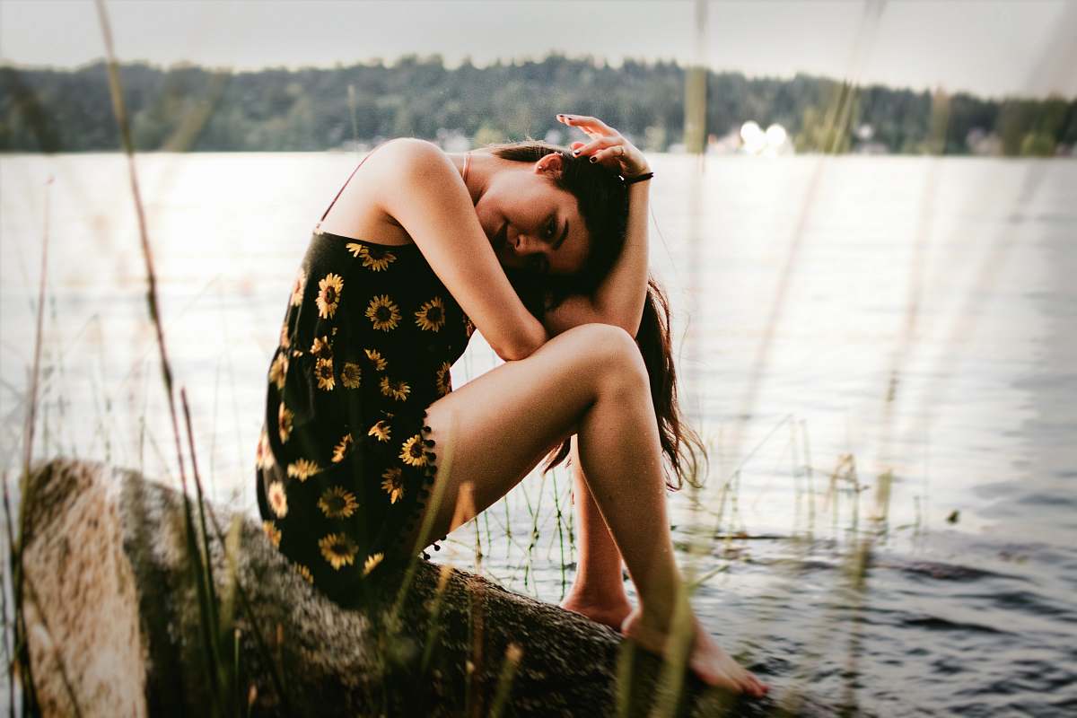 human woman sitting on rock near water person