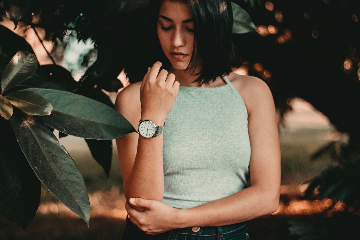 human woman standing near green leaf tree while holding her elbow with her right arm person