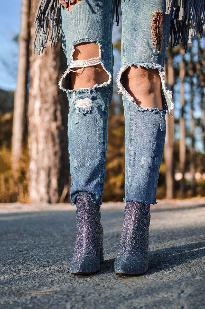 human woman wearing distressed blue denim jeans and pair of purple glitter booties jeans