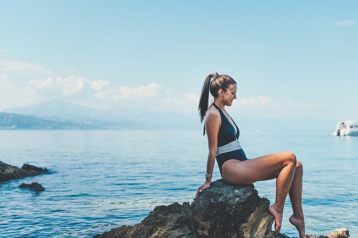 human woman wearing monokini sitting on brown rock near shore person