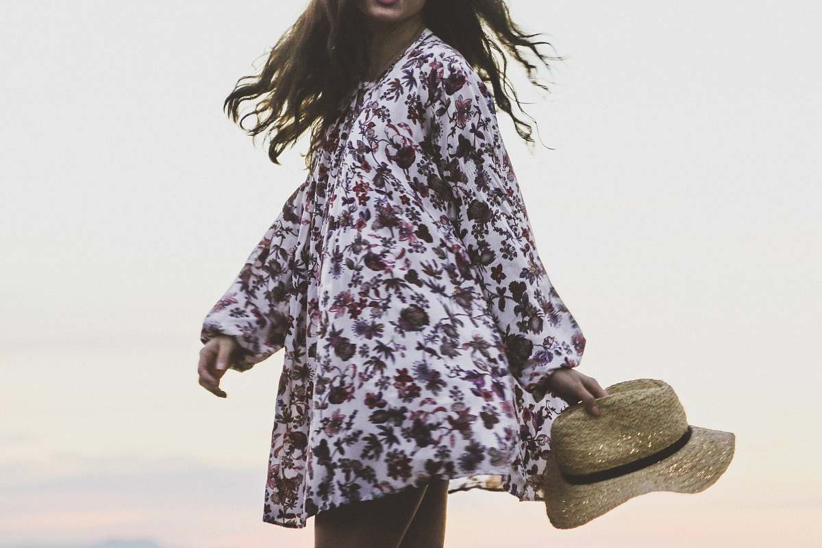 human woman wearing white and brown floral long-sleeved shirt while holding brown fedora hat person