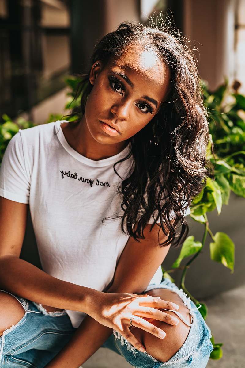 human woman wearing white crew-neck t-shirt and distressed blue denim bottoms taking photo near green plant at daytime person