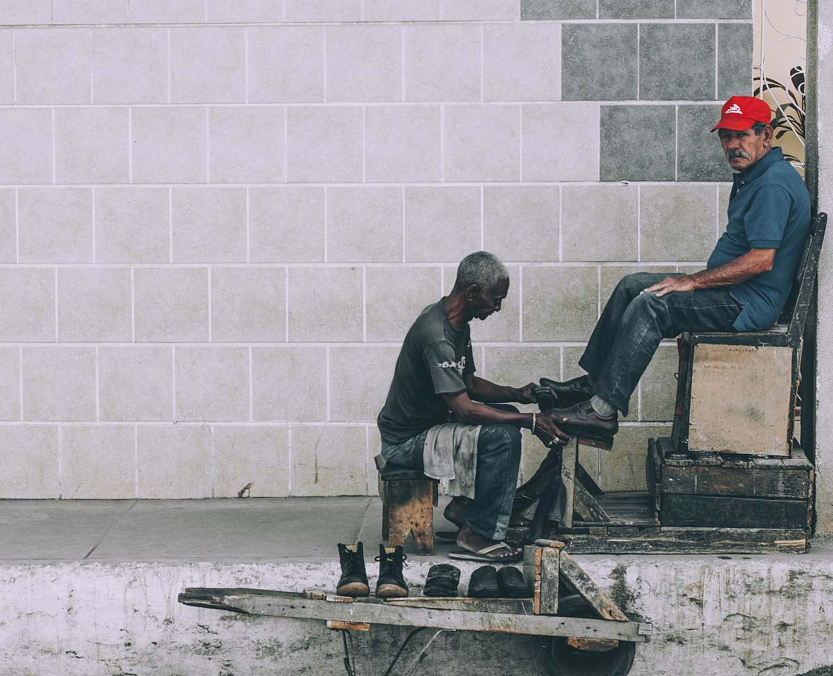 human man sitting on stool cleaning shoes at the alley people