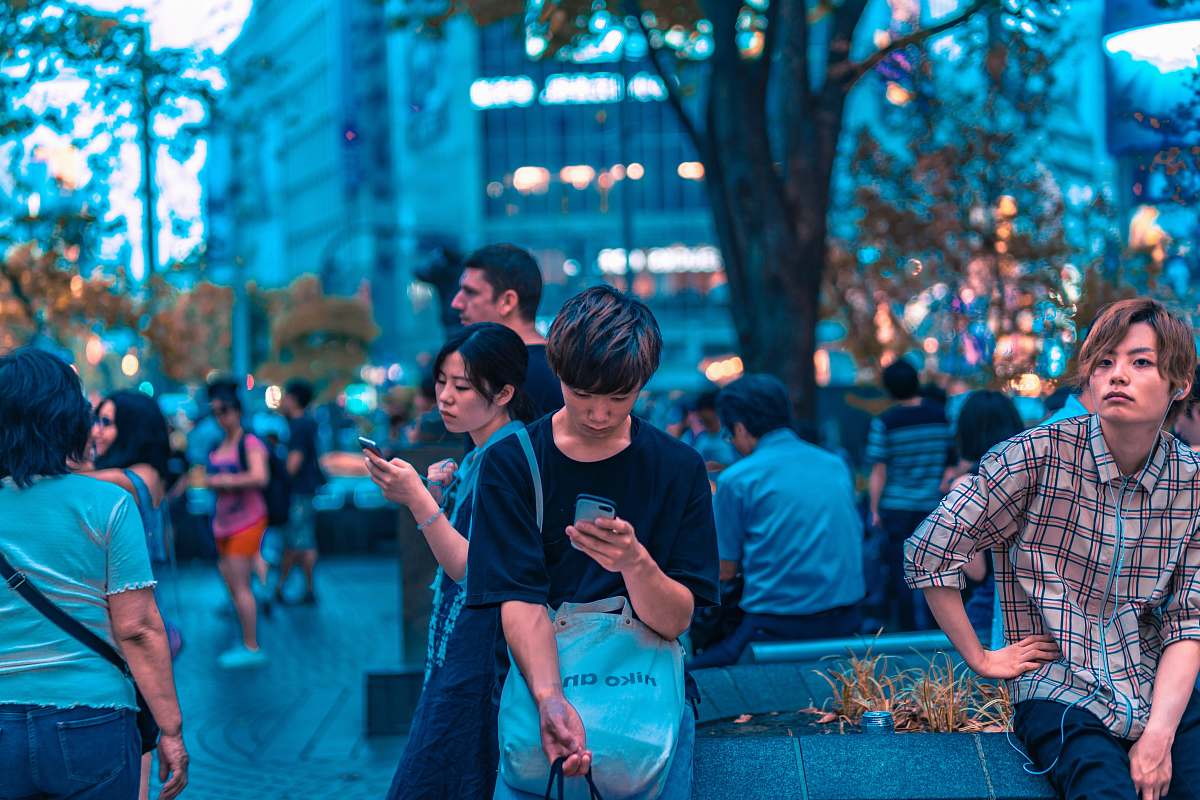 people selective focus photography of man sitting on concrete chair while holding smartphone human