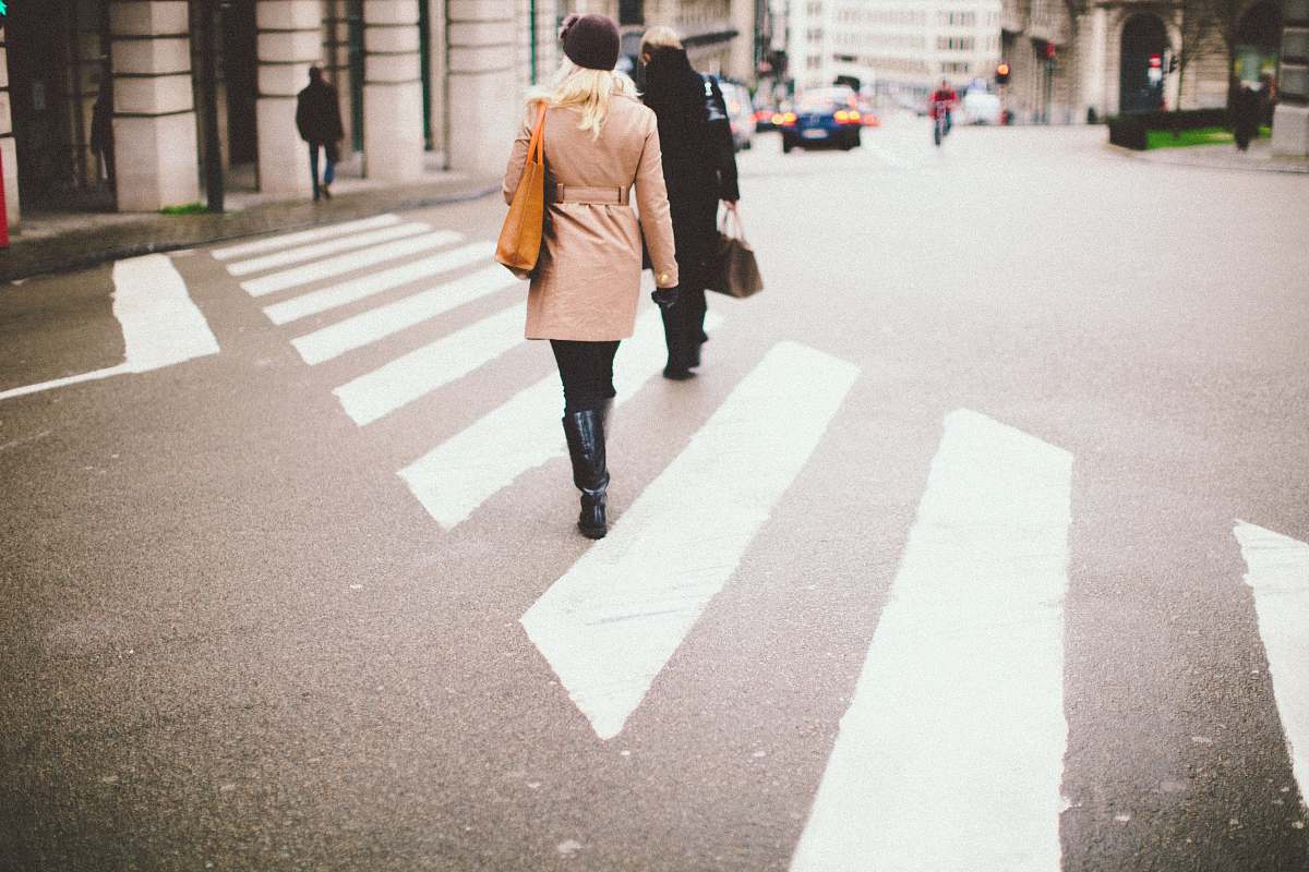 human two people walking on pedestrian lane towards gray concrete pillars during daytime photo people