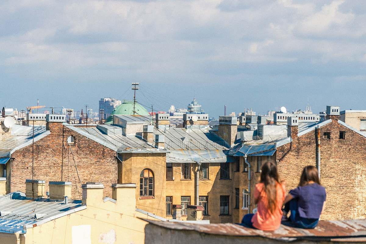 human two women sitting on roof overlooking building during daytime people
