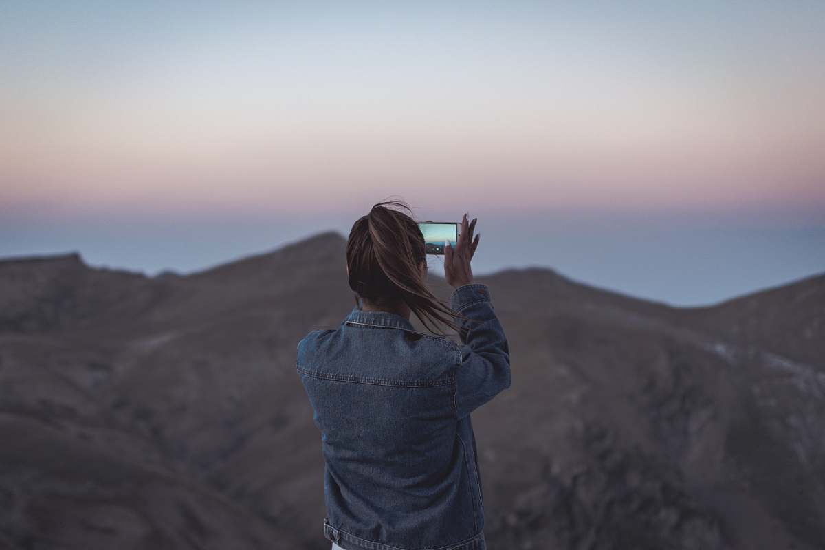 human woman in blue denim jacket taking picture of mountain people