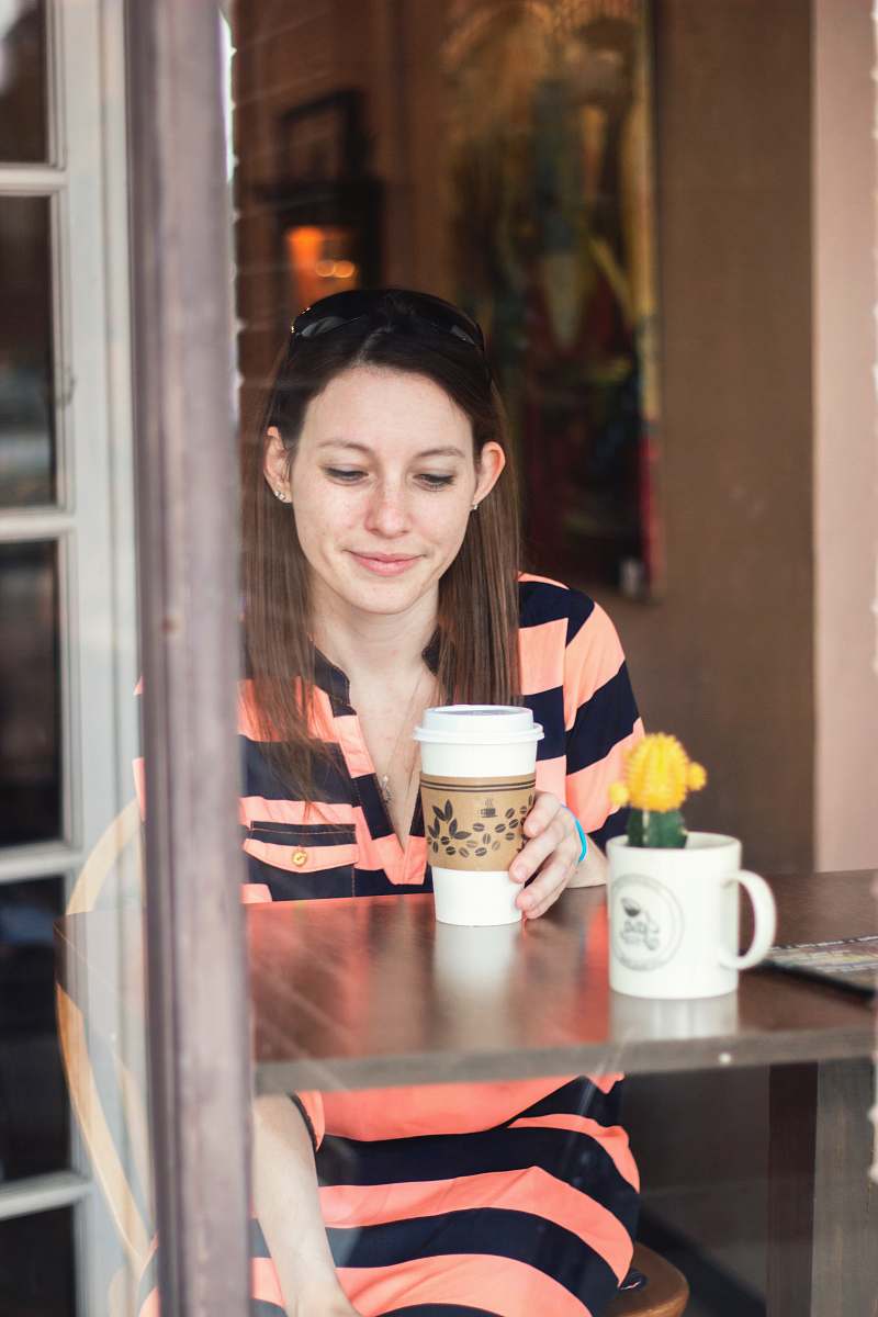 people woman sitting down at table looking at cup in hand cup
