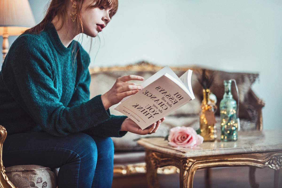 people woman sitting down near table reading 101 Essays book human