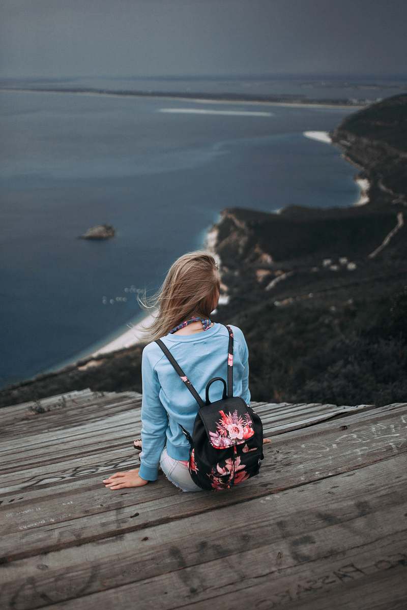 people woman sitting on brown plank facing body of water human