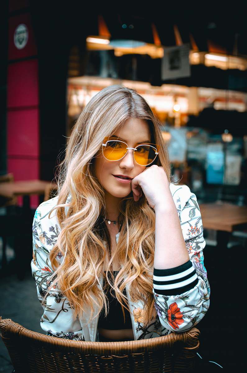 people woman sitting on brown wicker chair holding her face wearing multicolored floral zip-up bomber jacket human