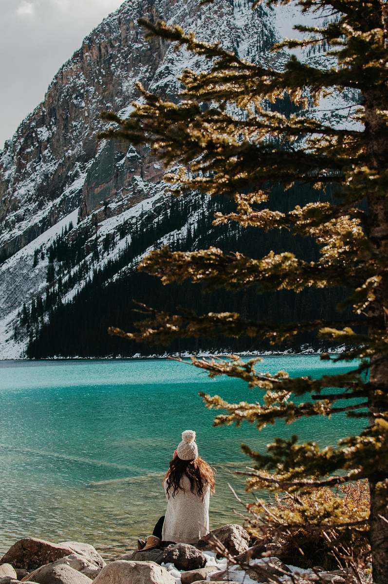 people woman sitting on stone facing body of water and glacier mountain during day human