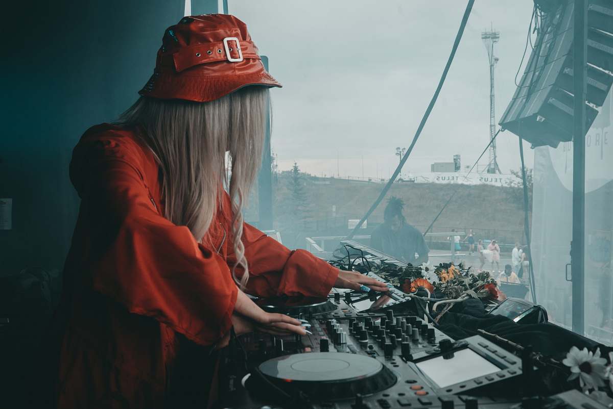 clothing female DJ in red blouse using black DJ software controller during daytime hat