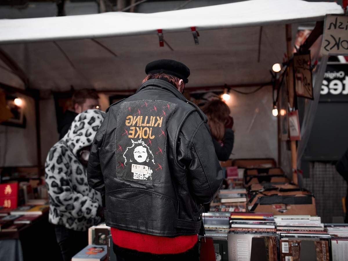 clothing man in black and white jacket and red pants standing in front of brown wooden table coat