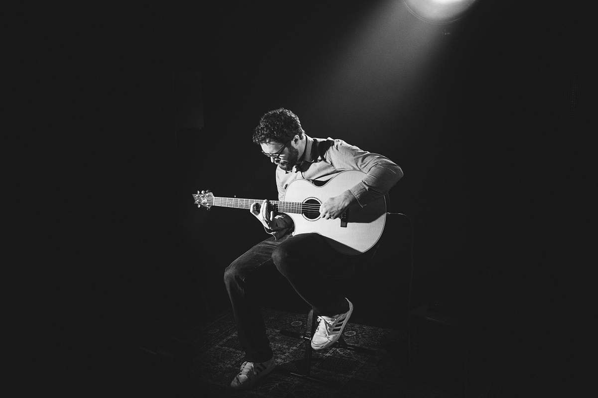 music grayscale photo of man playing guitar on stage guitar
