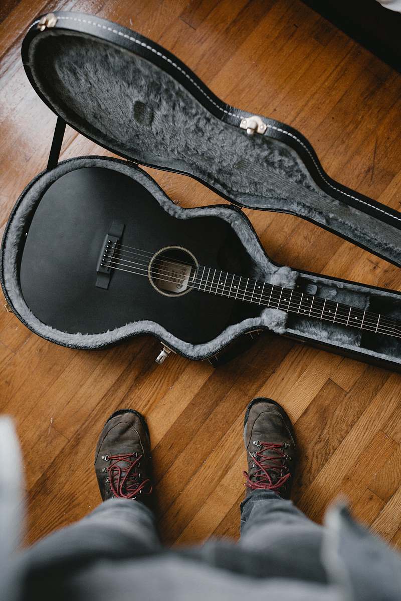 clothing person taking picture of black classic guitar inside black and gray guitar case cowboy boot