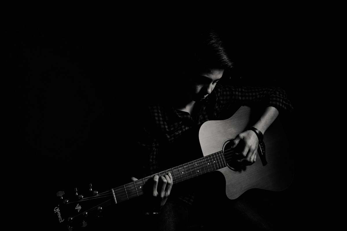 black-and-white man playing guitar on black background guitarist