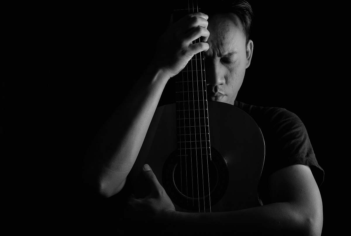 person grayscale photo of man hugging acoustic guitar black-and-white