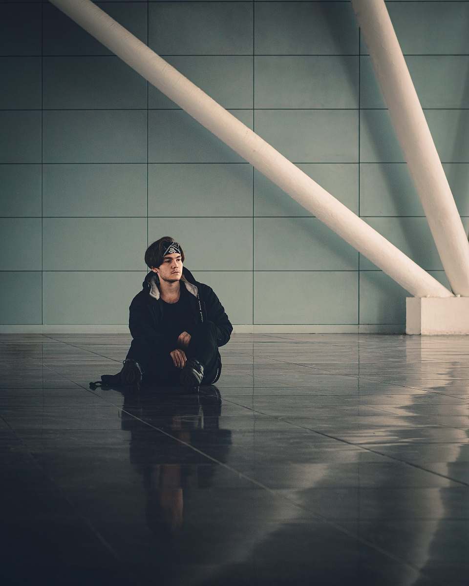 person man in black jacket sitting on brown wooden floor flooring