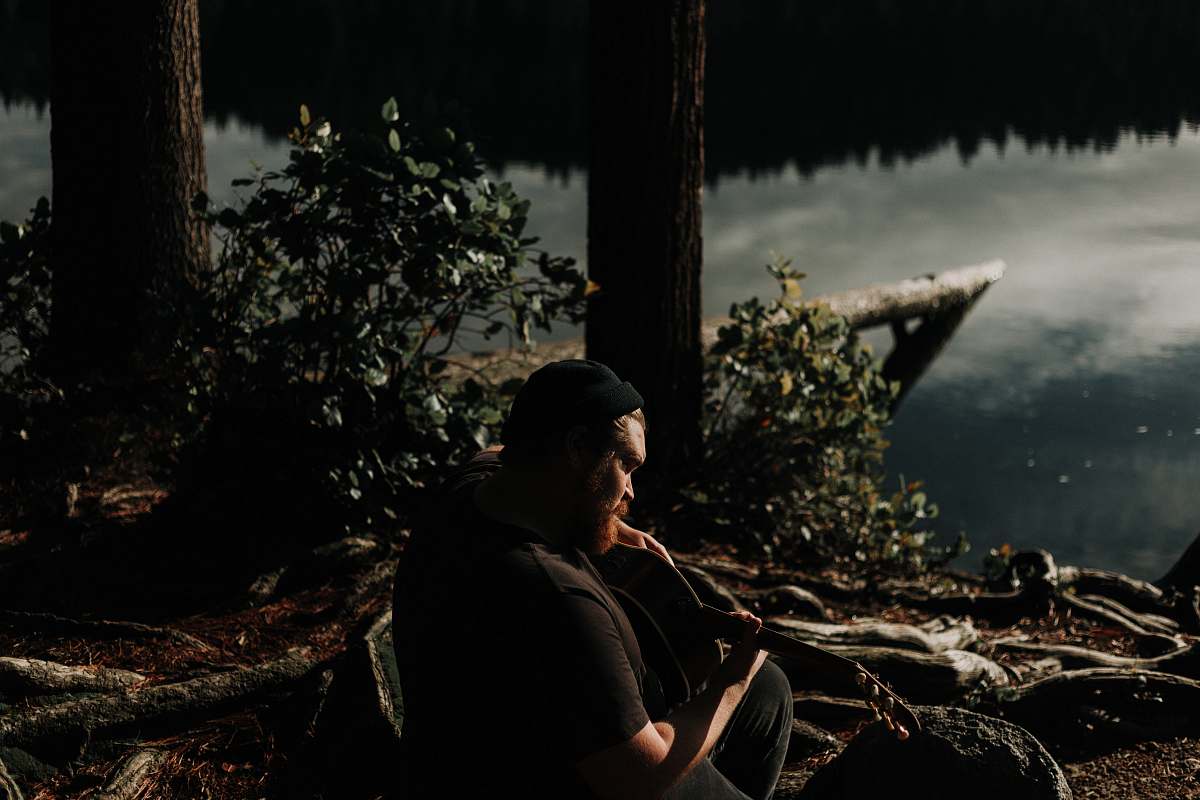 person man playing guitar near trees and and body of water nature