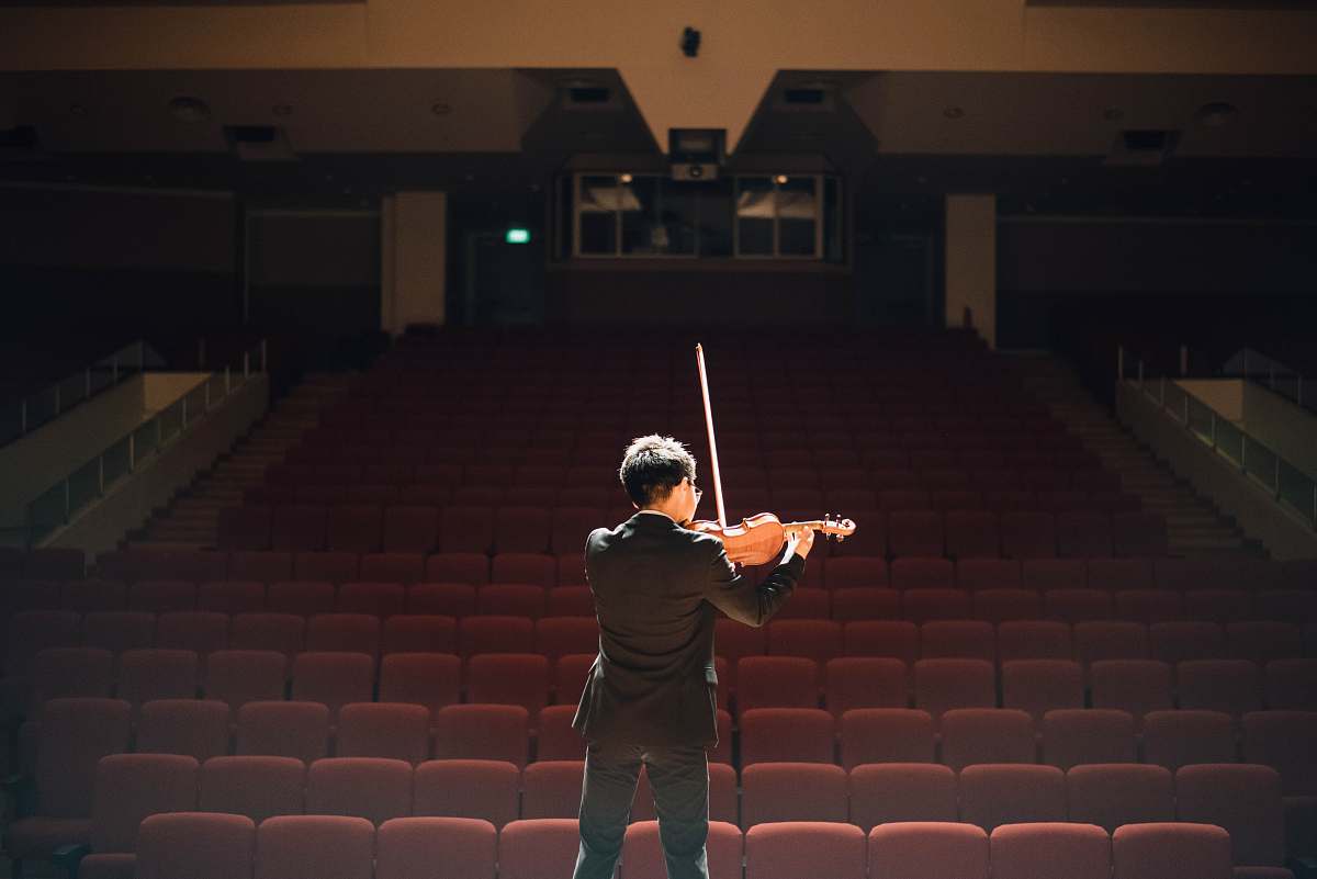 person man standing in front of stage playing violin people