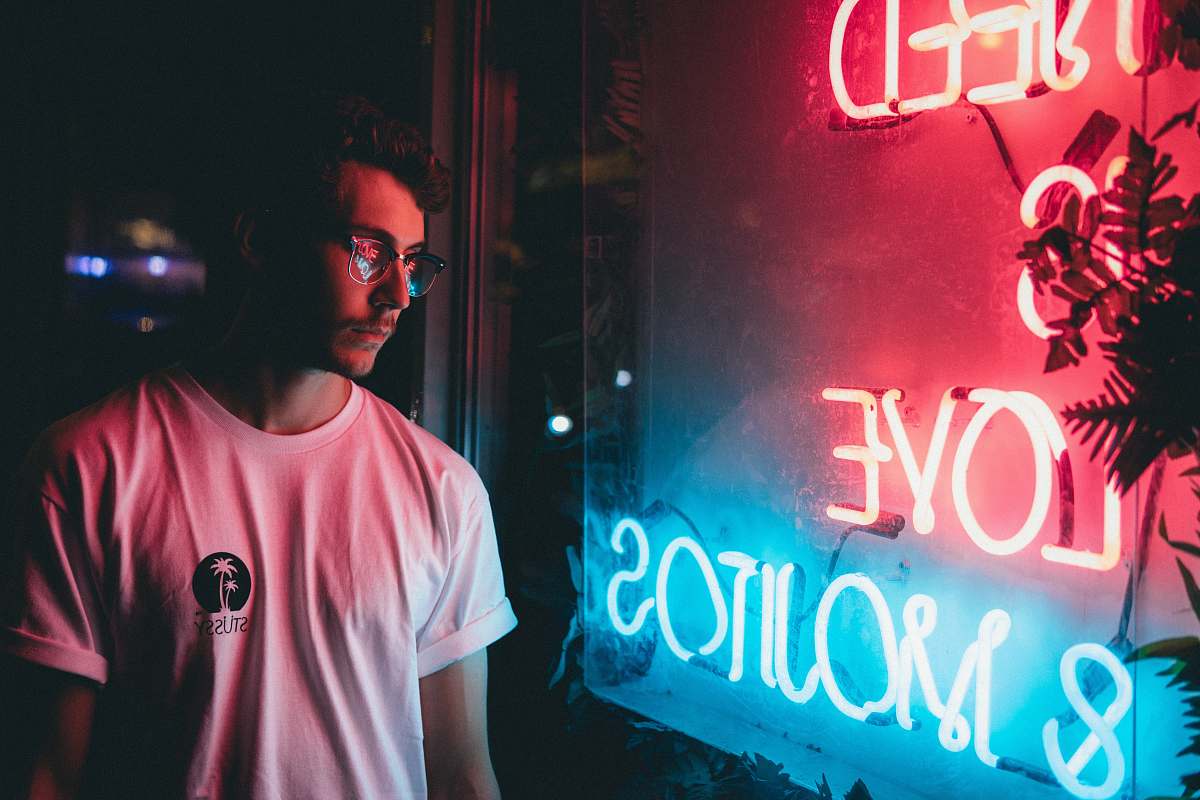 person man standing near red and blue neon signage people