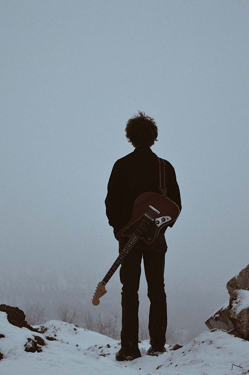 person man with guitar on his back standing on cliff people
