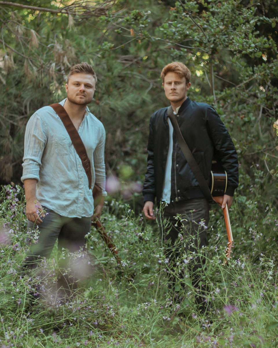 person two men with guitars standing in forest plant