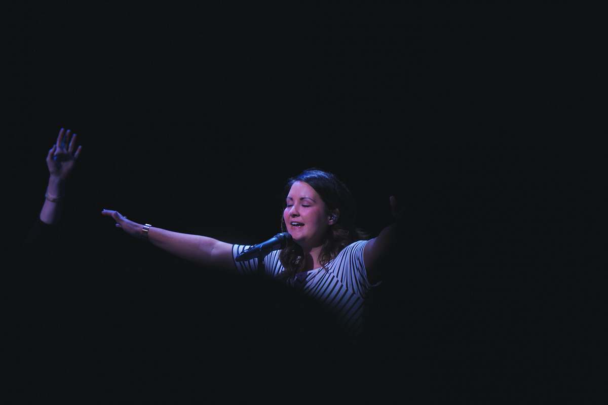 person woman singing on stage raising her hands performer