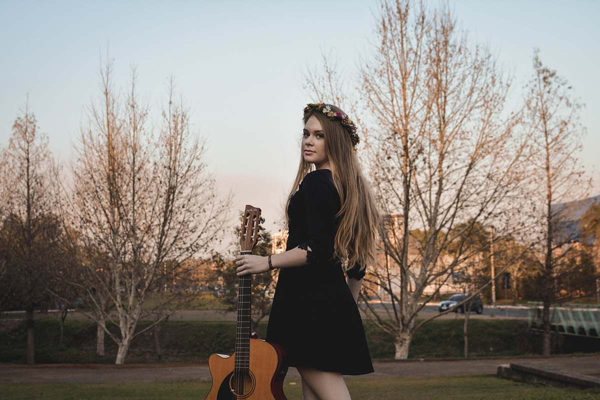 person woman standing on lawn while holding classical guitar woman