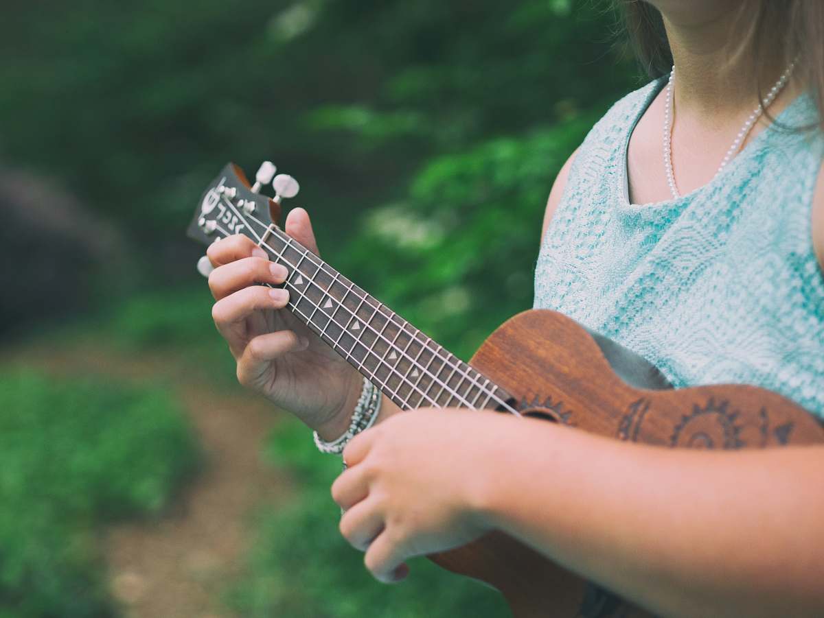 music woman wearing blue sleeveless top holding brown ukulele person