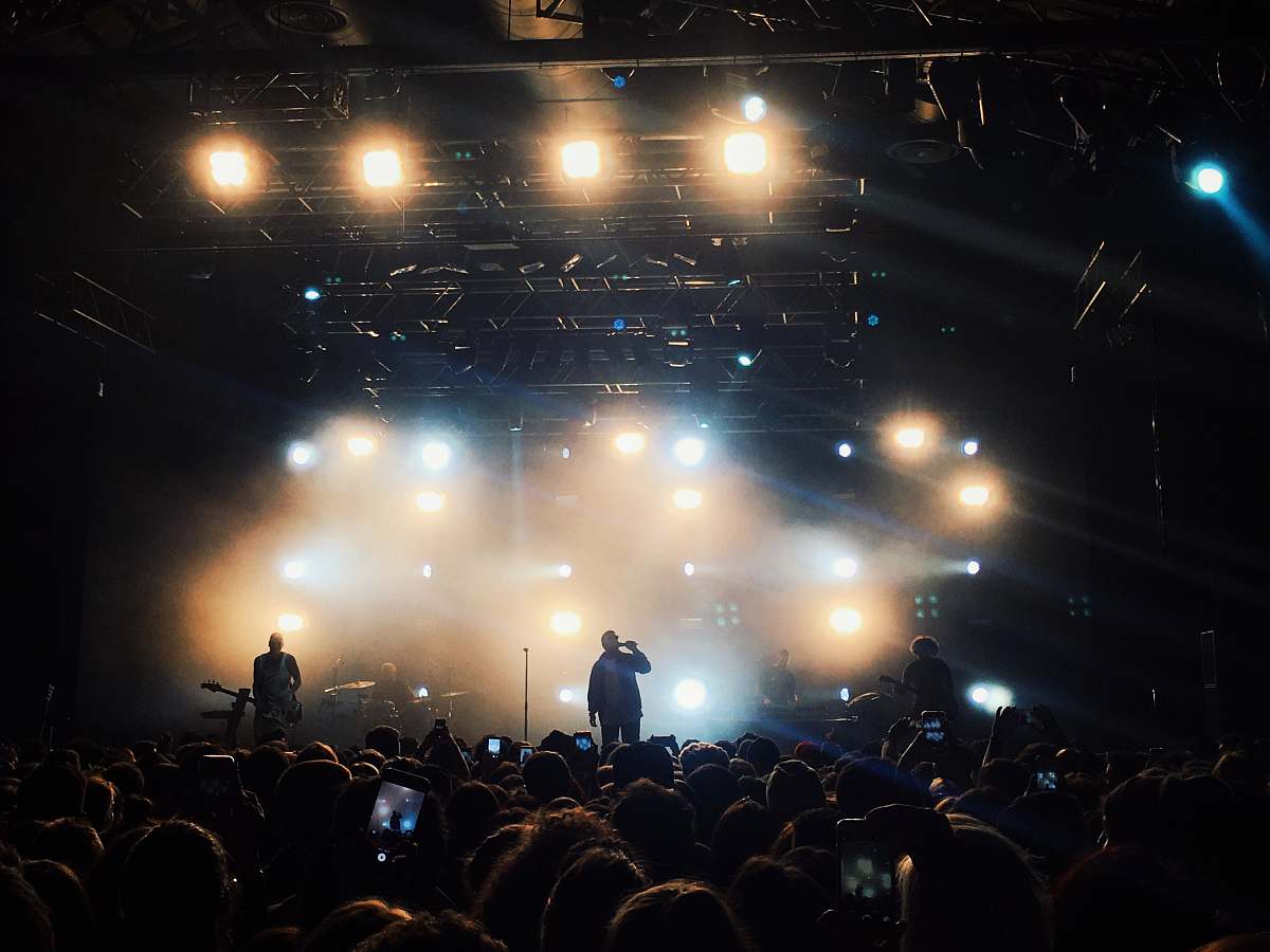 person band performing on black stage surrounded by people concert