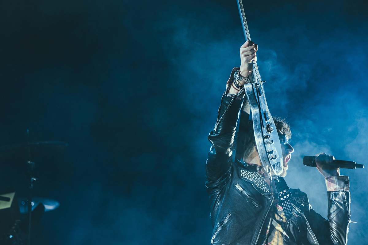 blue man holding electric guitar and microphone in front of lights inside dim room with smoke microphone