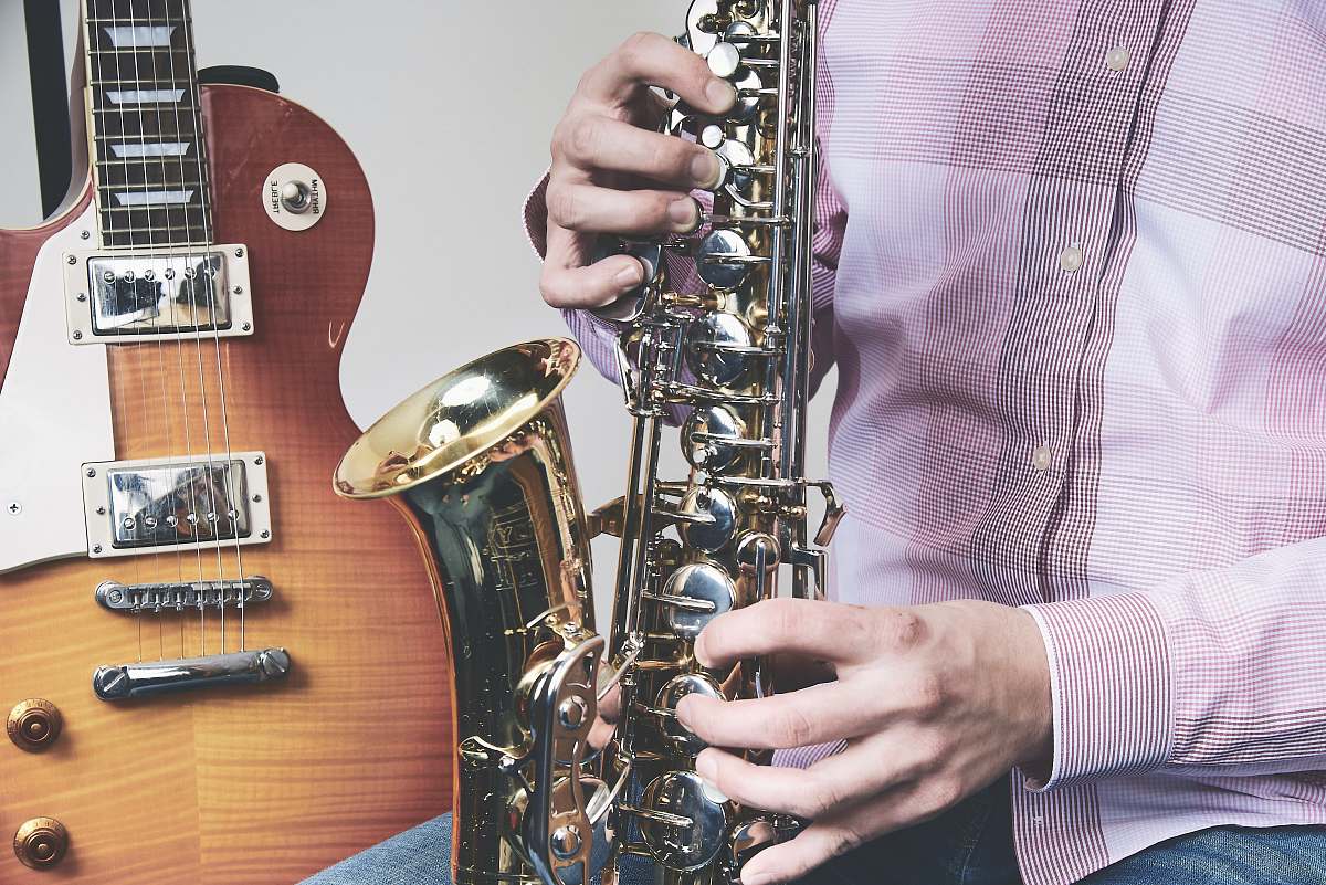 human man playing saxophone beside guitar guitar