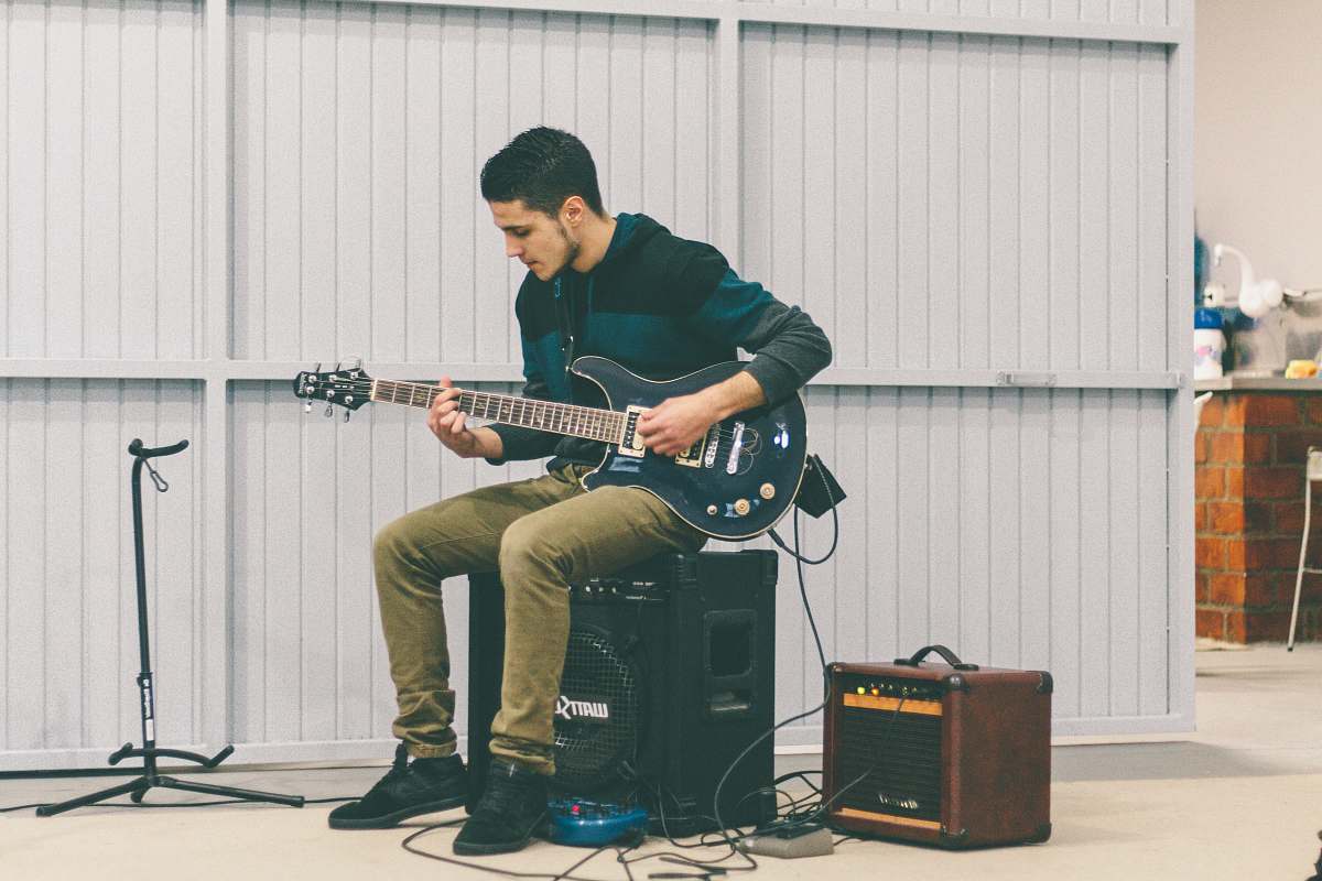 person man sitting in guitar amplifier while playing guitar at daytime guitar