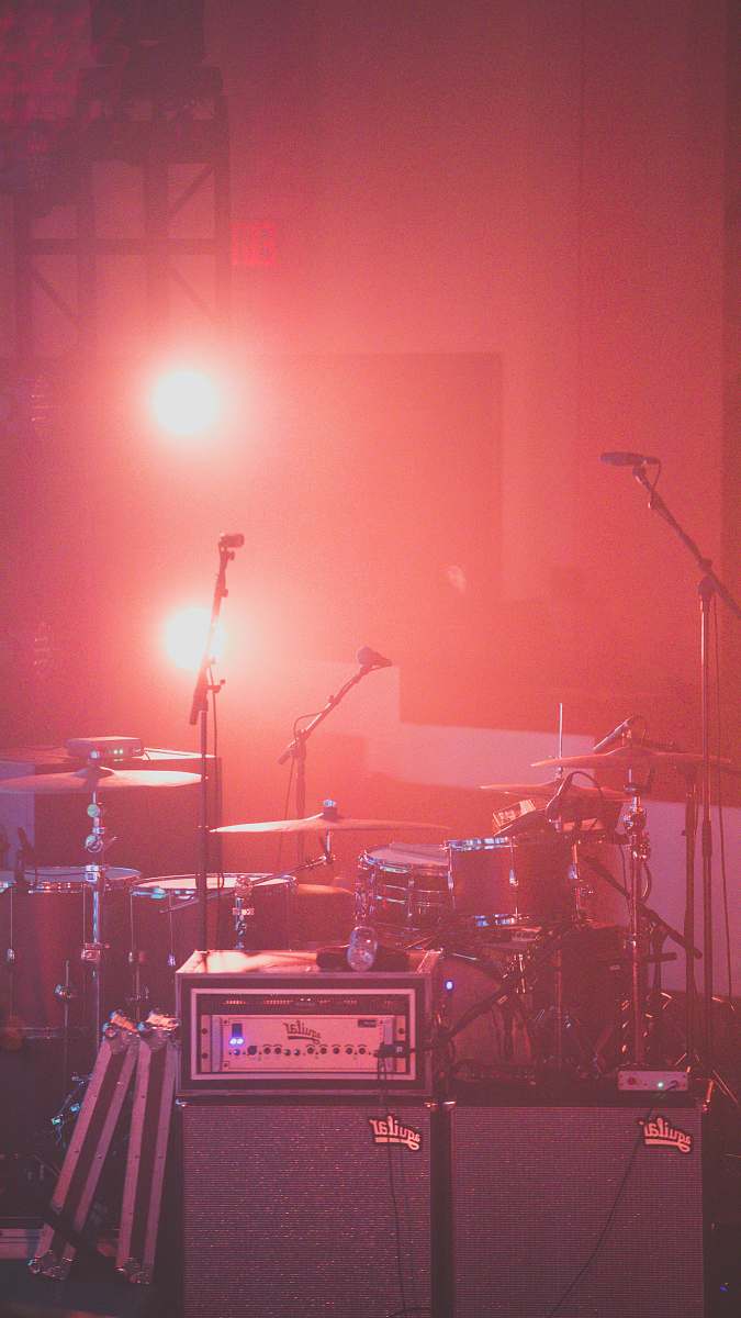concert red drum set besides microphone stands audience