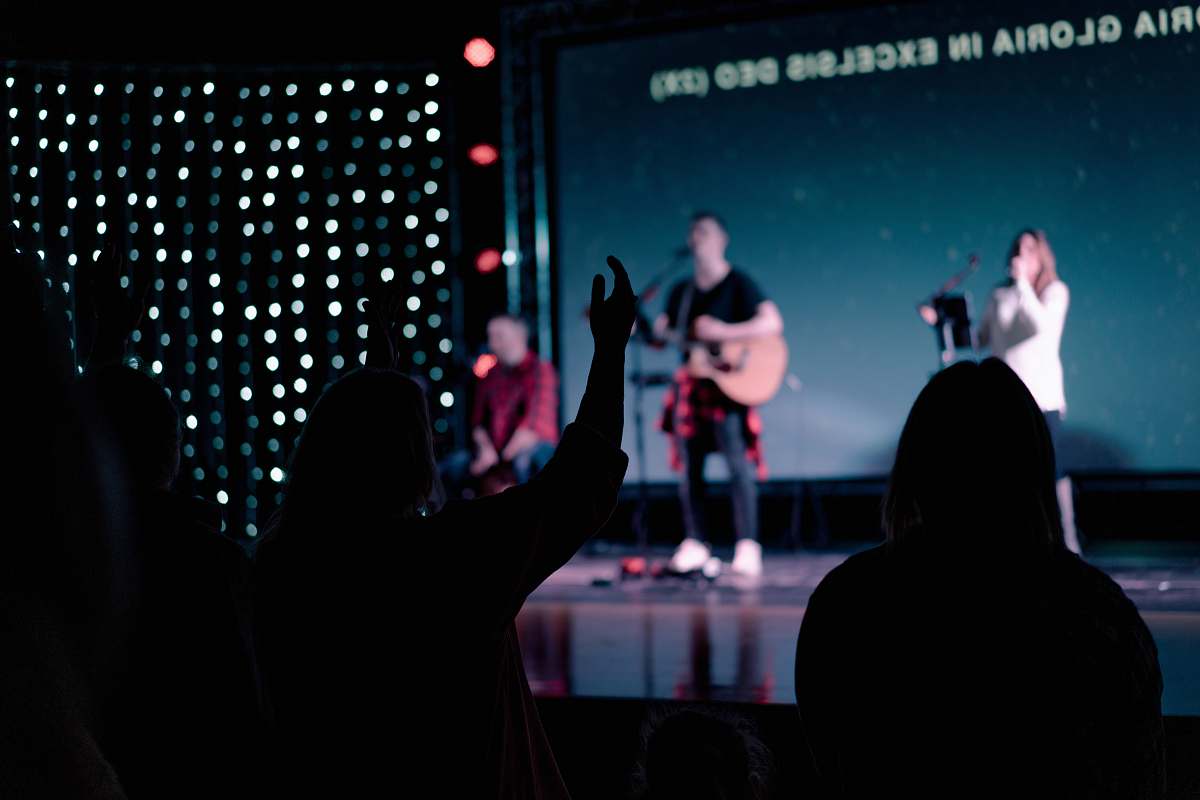 person man and woman on stage with people praising human
