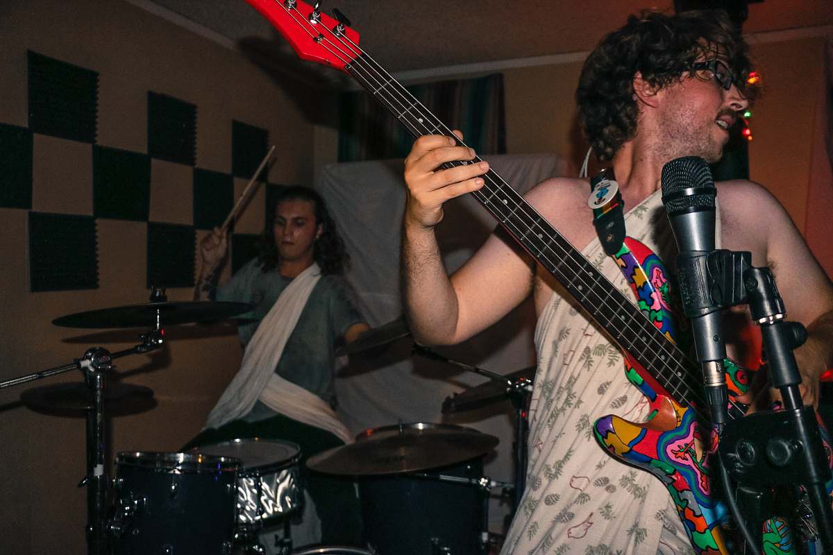 human man playing guitar wearing one-shoulder dress inside room person