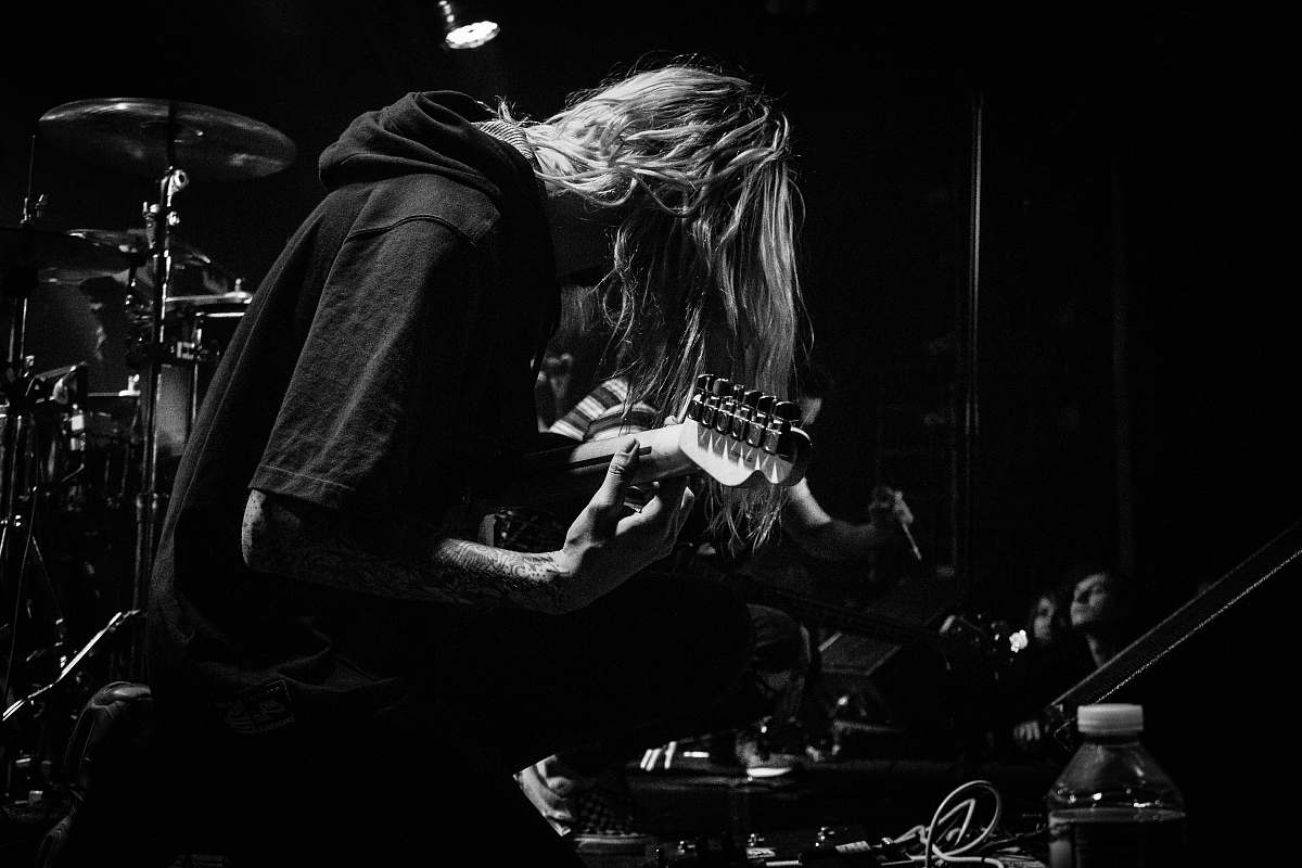 human grayscale photo of person playing guitar beside musical instrument black-and-white