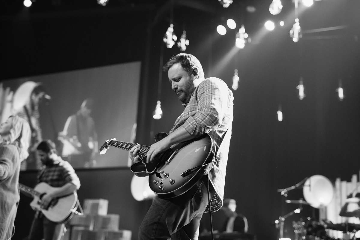 human greyscale photo of man playing electric guitar on stage black-and-white