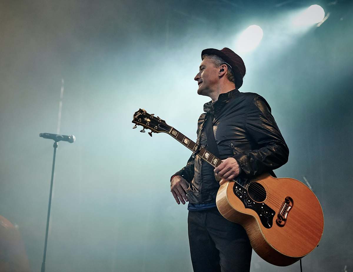 people man holding acoustic guitar beside microphone with stand musician