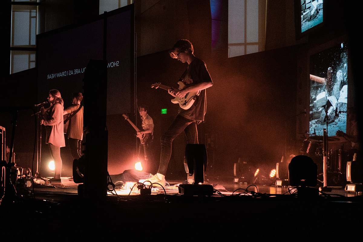 human man in black t-shirt playing guitar on stage musical instrument