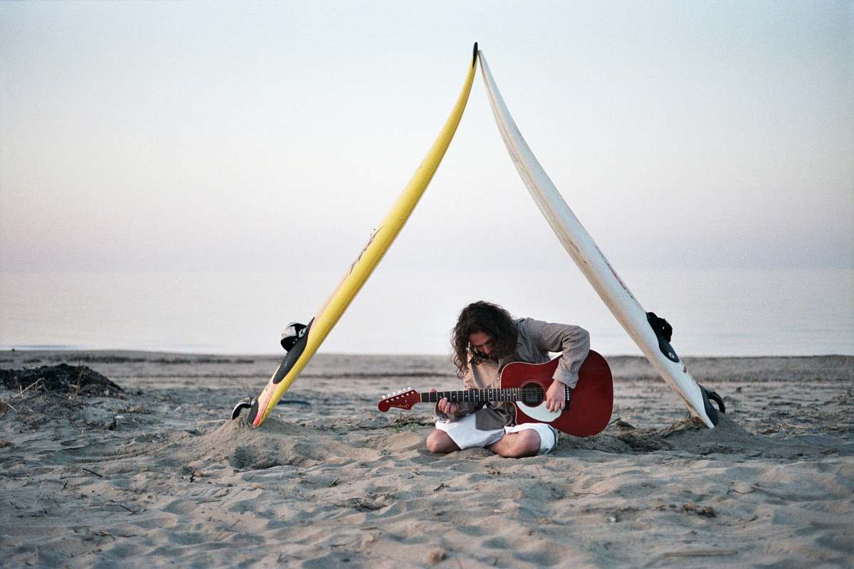 guitarist man playing guitar sitting on gray sand under cloudy sky guitar